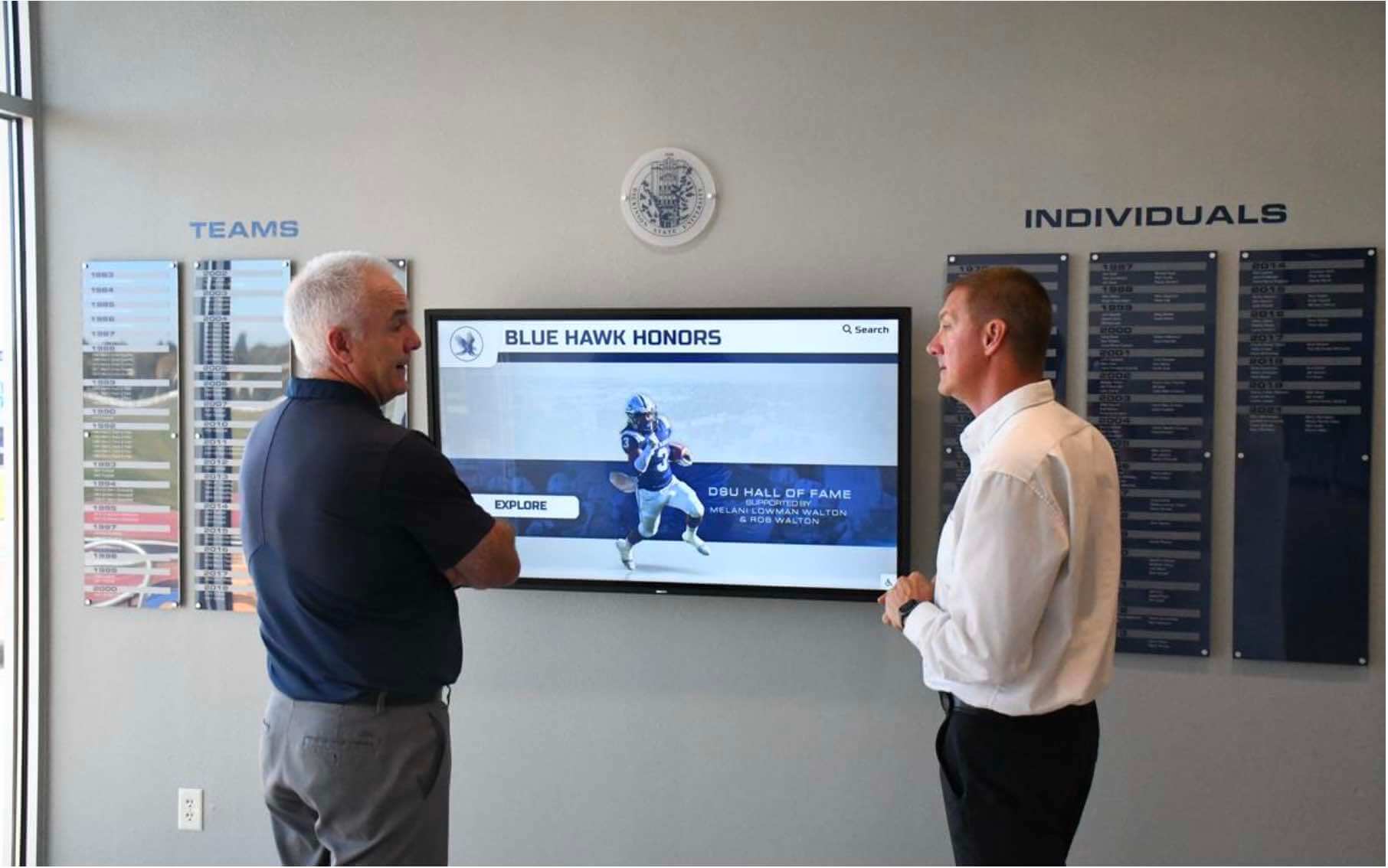 Visitors exploring digital hall of fame touchscreen display Two men viewing blue hawk hall of fame display